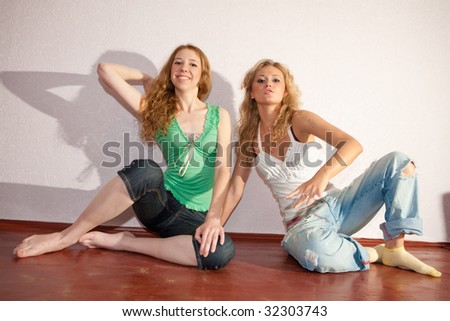 Two attractive young women sitting close on hardwood floor in home smiling and laughing.