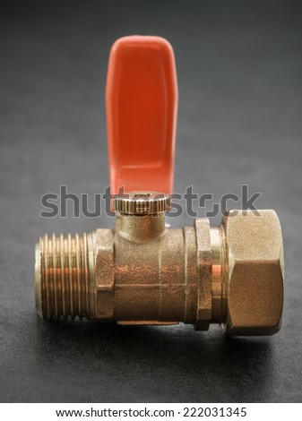 Ball valve with red handle on dark background. Selective focus with shallow depth of field.