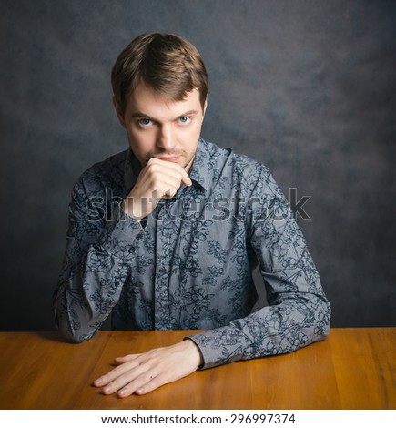 Handsome young man sitting at a table with his chin in his hand.