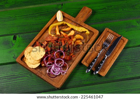 Mexican cuisine meat pieces in sauce with fried potato, onion rings, chips and jalapeno pepper on wooden board