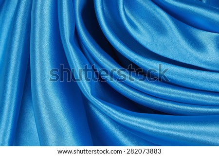 Blue Silk cloth of abstract backgrounds or wavy folds or satiny silk texture satin velvet material or elegant wallpaper design curve.