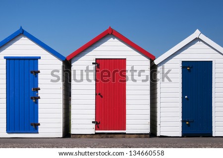 A set of three colorful beach huts at Paignton, Devon, UK on a sunny day.