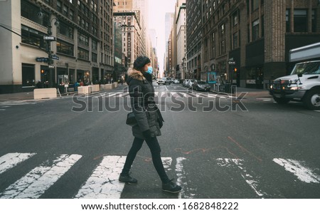 Woman wearing surgical mask going through crosswalk in midtown manhattan.Concept of Coronavirus, COVID-19 and quarantine