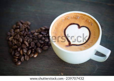 cup of coffee with latte art and heart coffee beans on wooden background