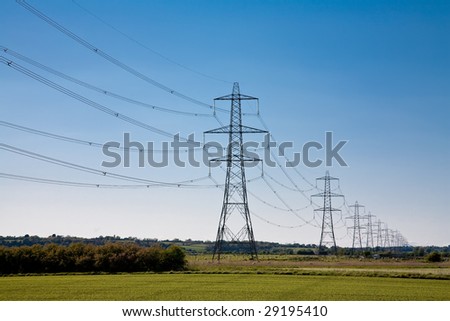 A wide angle view of Electricity Pylons crossing along a green field in East Sussex, England.