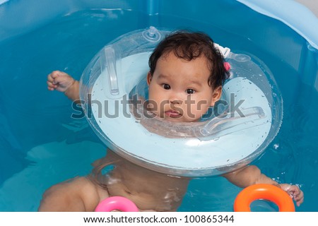 Baby swimming with neck swim ring in bath