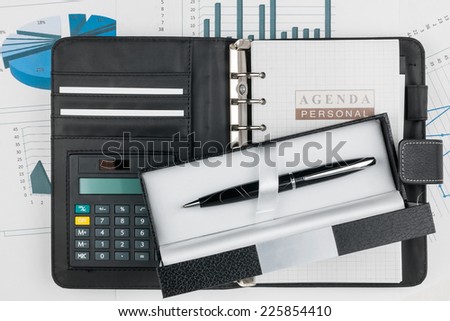 Diary, calculator and pen in the box on a background of diagrams and graphs,can be used as background
