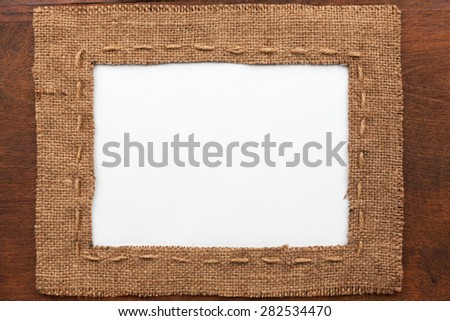 Frame made of burlap with white background lying on a wooden surface, with space for your text
