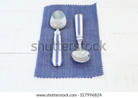 Two spoons with blue and white stripes handle on a blue napkin on an old white wooden table