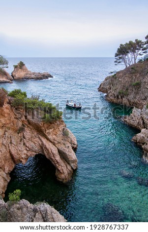 a small cove with crystalline waters and with a small cave, a small boat is sailing in it with three people, Cala de Sa Foradada, Palamos, Costa Brava, Girona, Spain Foto stock © 