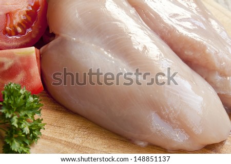 raw chicken breast sitting on wooden cutting board,white meat with parsley and tomatoes