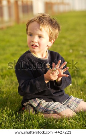 Little boy sitting in the grass picking clover with a cute expression on his face