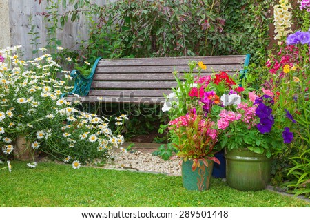 Cottage garden with wooden bench and flowers in containers.