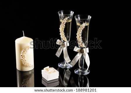 glass with champagne, candle and boxes for wedding rings on black background