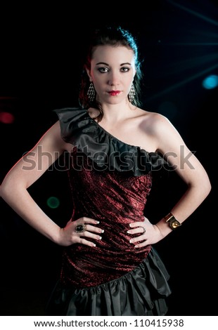 Beautiful young woman wearing black and red satin off the shoulder dress with stage lights