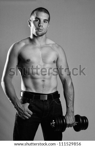 Attractive young man holding barbell with strong abs in black and white