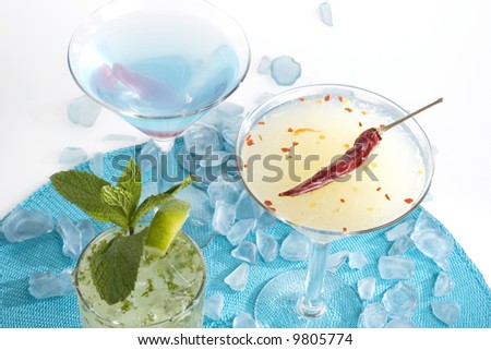 A Chili Cosmopolitan, Mediterranean Martini, and a Mojito on a blue background with glass shards.