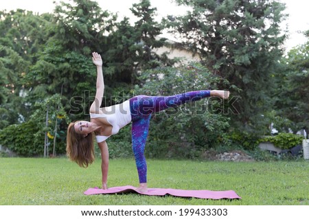 Beautiful young yoga instructor doing yoga on a green grass