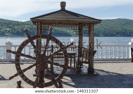 Wooden arbor with table and decorative helm on the Angara river shore