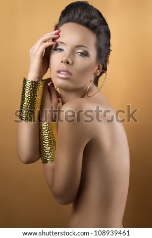nude sexy girl with two big golden bracelets and hoope earrings, she is turned of three quarters, looks in to the lens and her hands are near the face