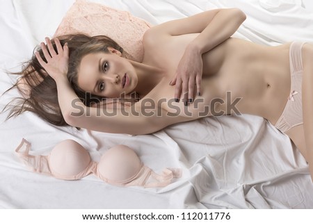 Sexy girl lying on the bed with her bra placed next, her right hand is on the head and her left hand is on the breast, she looks in to the lens