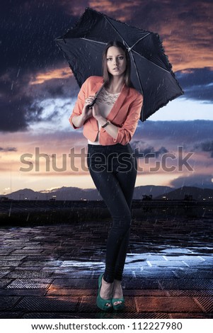 pretty young woman with dark umbrella, she is in front of the camera and looks in to the lens
