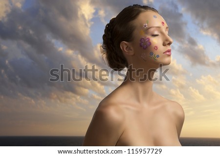 very pretty girl with naked shoulder and floral make-up ok her face, she is turned of three quarters at left with closed eyes