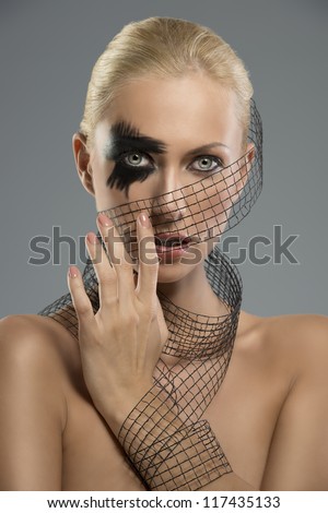Pretty blonde girl with dark make-up and grid around the neck, the face and wrist. she looks in to the lens and her left hand is near the face
