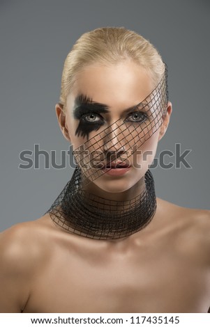 Pretty blonde girl with dark make-up and grid around the neck and the face, she is in front of the camera and looks in to the lens