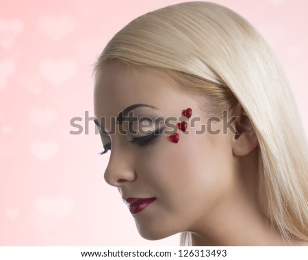 pretty blonde girl with sexy clothing and heart shaped decoration on the face, her face is turned at right and she looks down at right