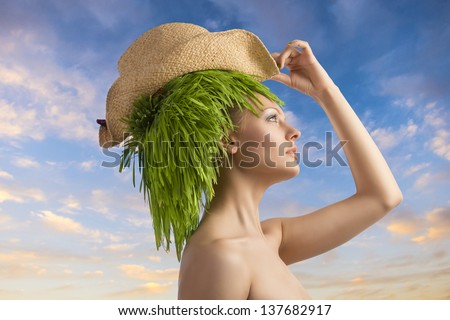 fresh portrait of beauty girl with green grass on hair-style, straw hat and naked shoulders on color cloudy sky