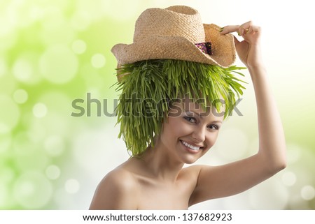 pretty young woman with summer hat and hair style done with some green grass smiling on color background