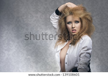 sexy rock blonde woman with opened shirt, dark glossy make-up and voluminous hair-style, looking in camera on old fashion background