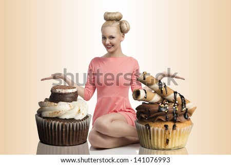pretty blonde girl with colorful make-up and creative hair-style sitting on the floor and shows two big cupcakes . Looking in camera and smiling