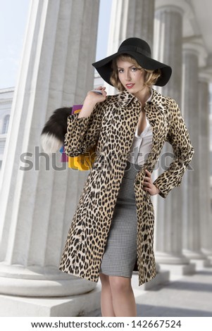 Blonde girl with showy look taking shopping bags and wearing leopard coat and big black hat