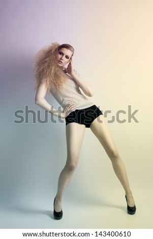 Cute blonde woman with creative hair-style in fashion pose wearing shirt with pois pattern, black shorts and heels