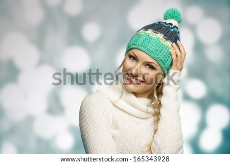 pretty young woman looking in camera and smiling , wearing a white wool sweater and winter green hat