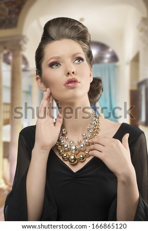 fashion shoot of pretty young brunette girl with elegant style, beautiful hair-style, black dress and big necklace