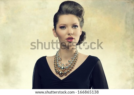 portrait of aristocratic fashion female posing with elegant hair-style, black dress and big necklace. Looking in camera with sensual eyes