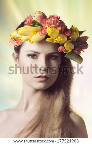 beauty close-up portrait of cute young lady with spring floral style. Looking in camera with colorful make-up and wearing floral spring garland on her head