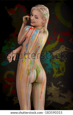 beautiful blond nude girl with multicolored body paint over her body smiling with sexy pose against gray background.