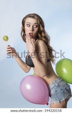 sexy summer posing in funny summer shot with colorful balloons. Posing with long hair, bikini and shorts, eating lollipop