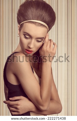 beautiful woman in fitted cream and black dress is looking down. She has got big blue eyes, brown big hairstyle and she is wearing hairband and pearls on her ea