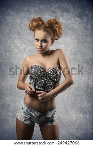 glamour fashion portrait of redhead woman with trendy sexy style and creative pigtail hair-style. She wearing provocative corset adorned by shiny gem and denim shorts