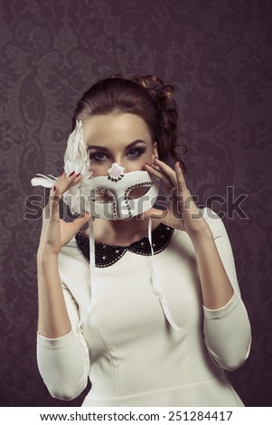 vintage portarit of elegant woman in white with carnival mask . she is posing at the camera .
