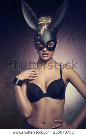 erotic easter dark portrait of very sexy blonde female with curly hair-style and black lingerie, wearing bizarre dark bunny mask on the face and looking in camera
