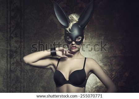 fashion Easter creative portrait of mysterious woman with blonde curly hair-style and lack bra posing with cute dark bunny mask. Fetish atmosphere