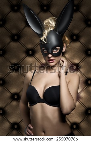 glamour easter shoot of very sexy blonde female with curly hair-style and black lingerie, wearing stylish creative dark bunny mask on the face and looking in camera