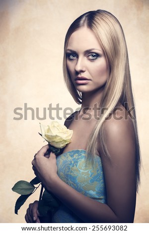 charming blonde woman with long silky hair posing with spring fashion dress and white rose in the hands