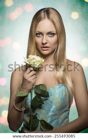 spring portrait of romantic blonde woman with long silky hair, wearing stylish dress and taking beautiful rose in the hand